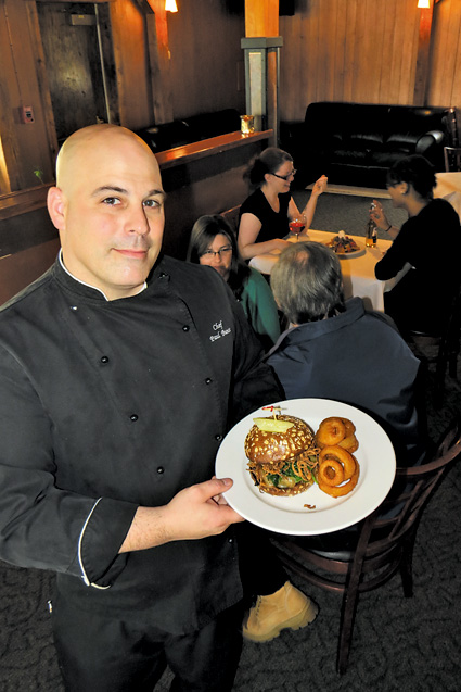 Water Street Landing chef Paul Bunce holds up the River SideBar's ghost pepper cheeseburger, which is paired with crispy onion rings (also shown inset with a plate of duck nachos).
