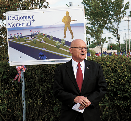 Patrick Soos of the DeGlopper Memorial Expansion Committee speaks during a groundbreaking ceremony last Thursday in front of a design of the proposed DeGlopper Memorial.