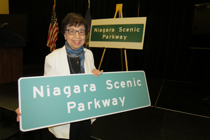 Mamie Simonson proudly displays the new parkway sign.