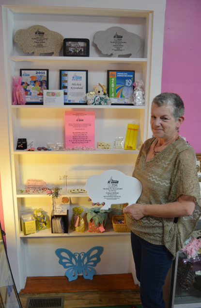 Michele Krienbuhl stands by shelves of merchandise at her business, Michele's Motif, where 100 percent of the sale is donated to the Roswell Park Cancer Institute.