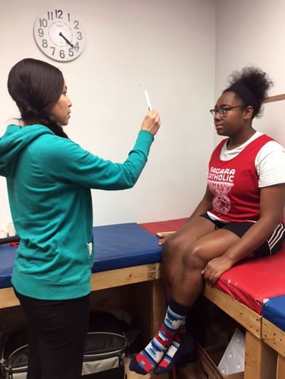 Ana Salgado, athletic trainer at Niagara Catholic Jr./Sr. High School, is shown assessing injuries of athletes Quasie Clarke and Jillian Lamb.