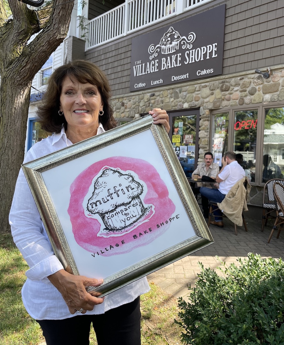 Maureen Kellick stands in front of the Village Bake Shoppe with one of the original watercolor paintings she made for the Lewiston sweet shop.