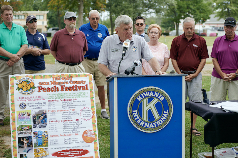 Peach Festival Advisory Chairman Jerry Wolfgang addresses the media. Local elected leaders and Kiwanians are shown in the background.