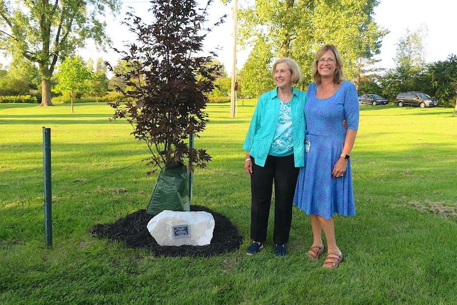 Dianne Tiede and Cyndi Booker at the newly planted tree with the plaque dedicated to Tiede's 22 years of coordinating Eco Island.