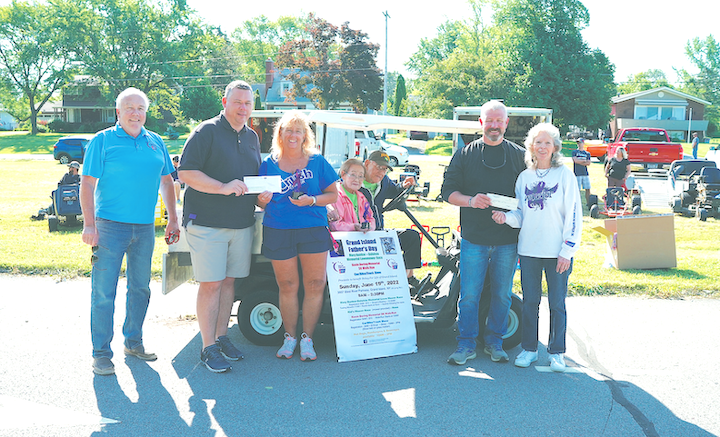 A great time notwithstanding, the Mary Dunbar-Daluisio Memorial Lawnmower Race raises money for worthy causes. Shown in a check presentation photo at the event, from left: Grand Island Town Supervisor John Whitney, Lynn Dingey, Chris Taylor, Floyd and Chie Doring, and Brian Runions with Mary Ehde. (Photo by K&D Action Photo and Aerial Imaging)