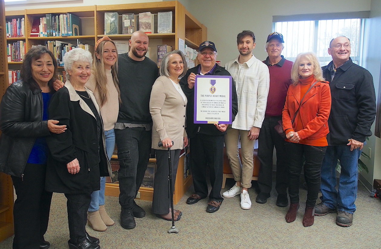 Ron Krul, of the Niagara Falls chapter of the Military Order of the Purple Heart, presents Morano's widow, Celeste, with a plaque honoring Morano's sacrifices, as family and friends look on.