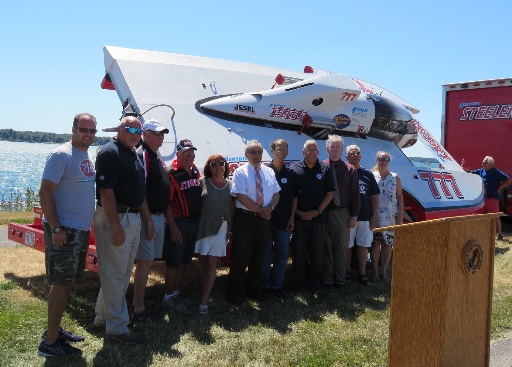 North Tonawanda city officials and Thunder on the Niagara sponsors pose for a group picture following Monday's press conference. In the background is an example of a hydroplane that will take the Niagara River for the event. (Photo by David Yarger)