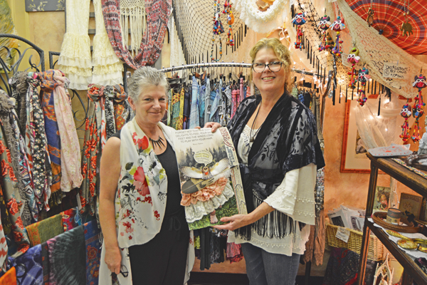 Holly Rankie, owner of Hip Gypsy, and Michele Krienbuhl, owner of Michele's Motif, display a sign for the Mother Earth celebration fashion show in front of clothing and accessories offered at Hip Gypsy, 102 Webster St.