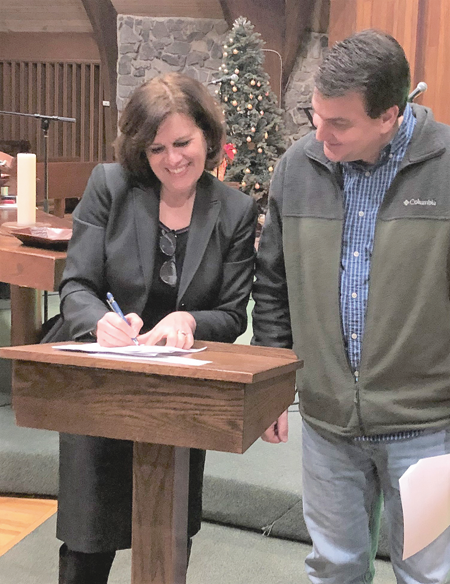 Mary Travers Murphy, left, president and CEO of Family Justice Center, signs the contract to rent the home that will be the FJC's next satellite office. She is joined by Trinity Church Pastor Kevin Slough. (Photo courtesy of Family Justice Center)