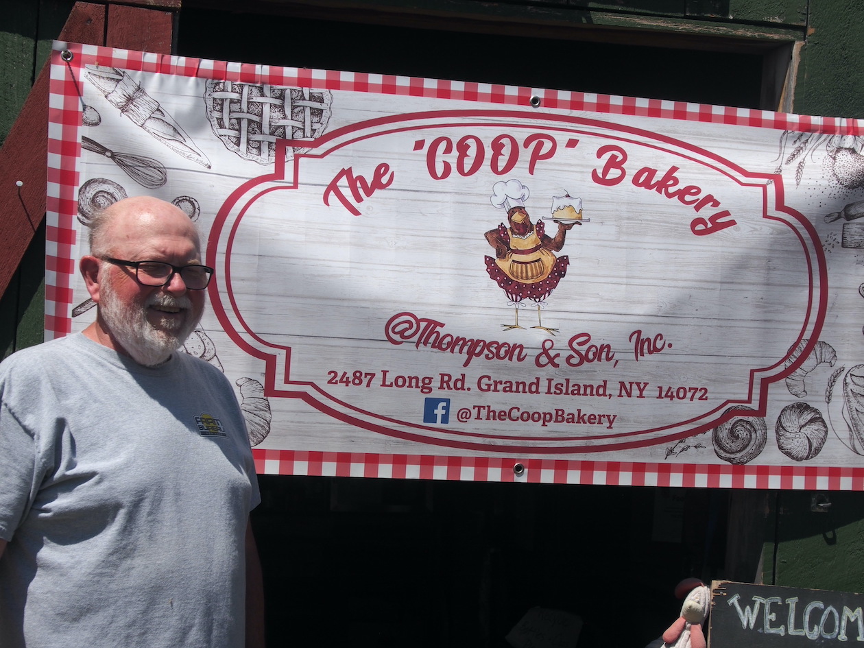 Tom Thompson stands in front of a sign advertising home-baked desserts, prepared by the Coop bakery.