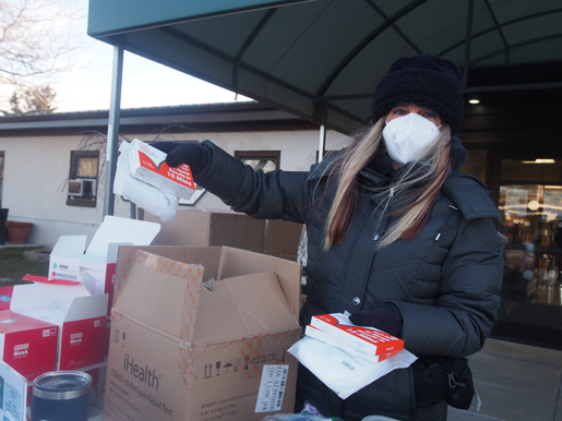 Jennifer Menter stands near the entrance of the Grand Island Golden Age Center, holding sets of masks and COVID-19 at-home antigen test kits.