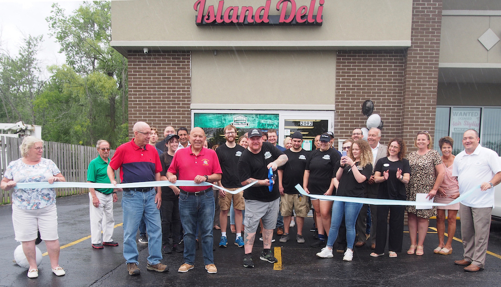 Twin City Island Deli owner James Zuckerman cuts the ribbon, surrounded by employees, town officials, and members of the Grand Island Chamber of Commerce.