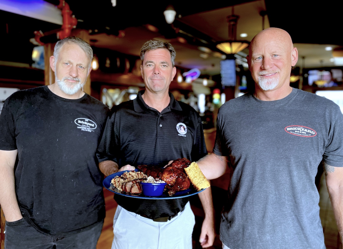 Pictured at the Brickyard Pub & BBQ are, from left, Steve Matthews, Ken Bryan and Eric Matthews. Bryan is holding `The Ultimate` platter, which includes a heaping mound of pulled pork, succulent half-rack of St. Louis-style ribs, tender brisket and a savory barbecued half-chicken. Served with two sides and cornbread, this mound of food is enough to feed a couple for a full week.