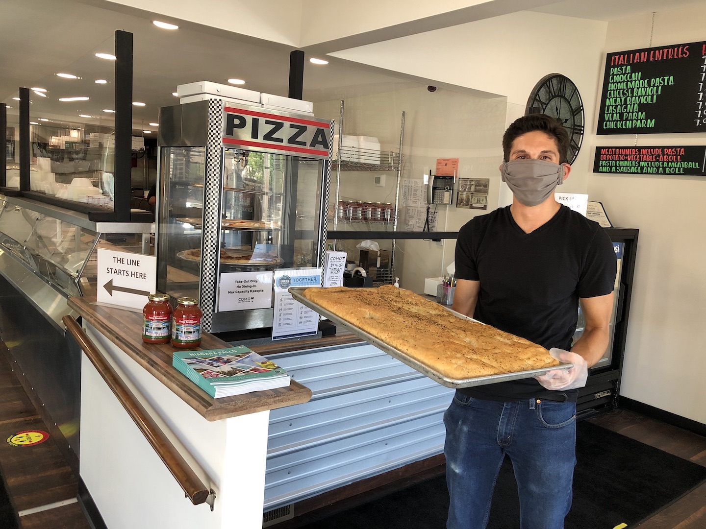 Dominic Colucci III (`Dom Jr.`) shows off a tray of the Como Deli's signature pizza bread. Around him are some of the new safety measures in place at the Lewiston eatery.