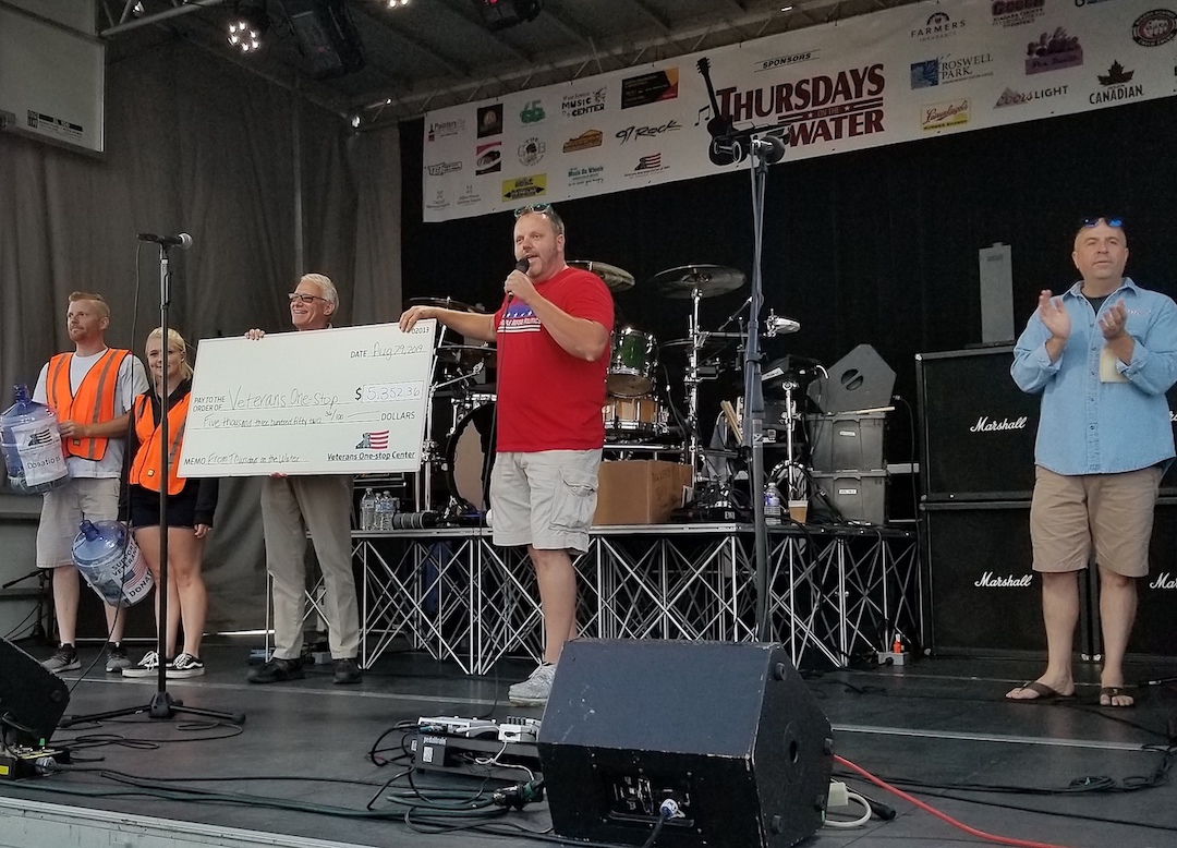 Niagara County Legislator Jesse Gooch (right, holding microphone) presents a check to Veterans One-stop President and CEO Chuck Marra (left, holding check).