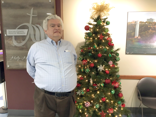 David Houghton, development director of Niagara Gospel Rescue Mission on Portage Road in Niagara Falls, stands next to Christmas tree at the entrance of the shelter.
