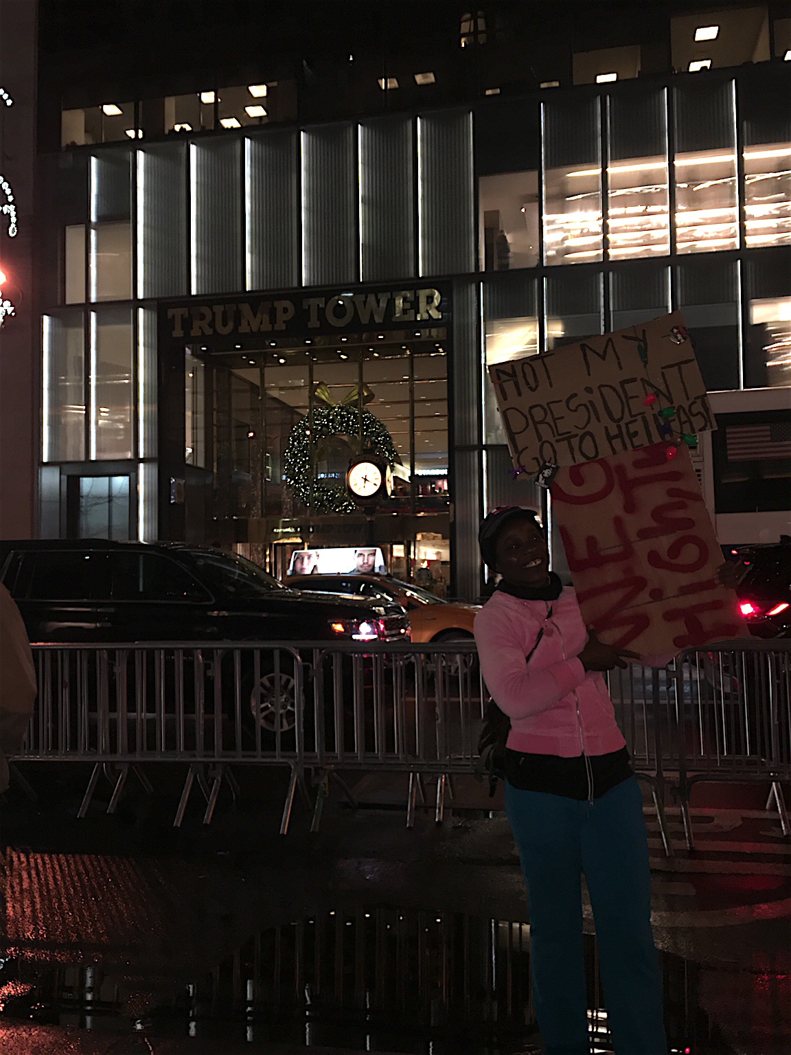 A woman holds a sign in front of Trump Tower stating, in part, 