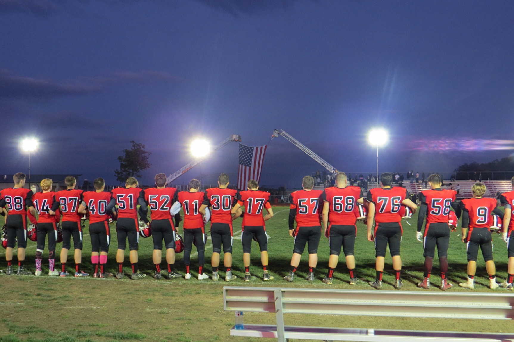 Niagara-Wheatfield football stands during the national anthem, as the flag waves between two fire trucks. (Photo by David Yarger)