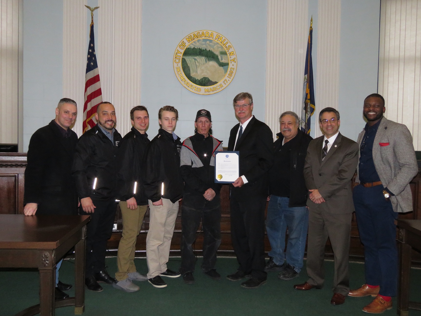 Representatives from the Niagara Falls Powerhawks and the City of Niagara Falls pose for a photo after the Powerhawks were issued a proclamation for their success in the 2017-18 season. From left: Niagara Falls Councilman Bill Kennedy, Powerhawks coach Jason Hill, Powerhawks captain Andrew Logar, Powerhawks defensman Matt Cavanaugh, Powerhawks Owner Steve Bueme, Niagara Falls Mayor Paul Dyster, Facility Operator Gene Carella, and Niagara Falls Councilmen Andy Touma and Ezra Scott. (Photo by David Yarger)