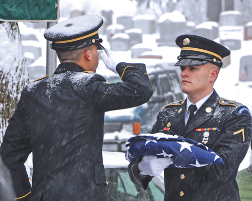 Spec. Christopher Roderiguez salutes as Pvt. Shelbi Vanderbogart holds a flag folded for presentation to the family of veteran Harold Smith during graveside services in Hudson on Dec. 17. (photo by Master Sgt. Corine Lombardo, New York Army National Guard)