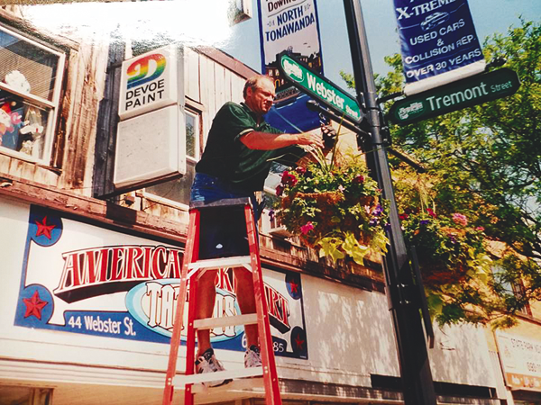 Volunteer Tom Peiper hangs a flower basket on Webster Street. (Photo courtesy of Project Pride)