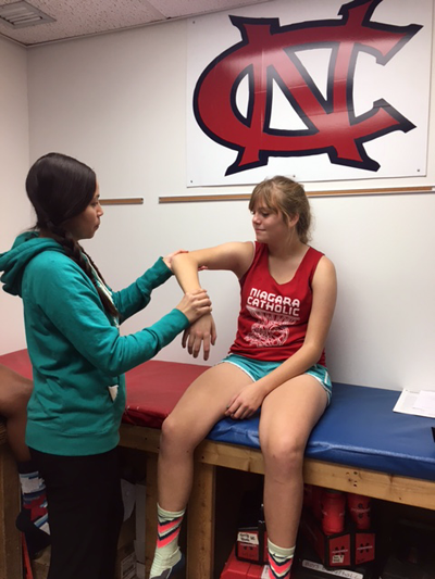 Ana Salgado, athletic trainer at Niagara Catholic Jr./Sr. High School, is shown assessing injuries of athletes Quasie Clarke and Jillian Lamb.